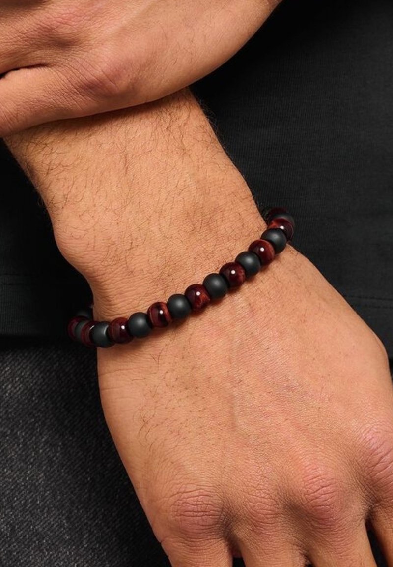 Bracciale di perline composto da perle nere opache e perle rosse scure lucide disposte in alternanza, appoggiato su una pelle chiara di un polso.
