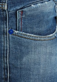 Jeans de mezclilla azul con un pequeño bolsillo frontal y costuras multicolores en rojo y verde, además de un detalle de botón azul en el bolsillo.