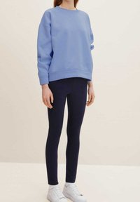 Felpa azzurra chiara con scollatura rotonda, maniche lunghe e vestibilità morbida, abbinata a leggings navy aderenti e sneakers bianche.