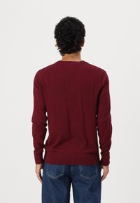 Pull à col rond bordeaux avec manches longues, poignets et ourlet côtelés, fabriqué en matériau doux, présentant une texture lisse et une coupe classique.