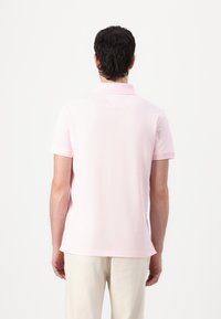 Lichtroze polo-shirt van zachte stof met een kraag, korte mouwen en een rechte zoom. Bevat een subtiele naaddetail aan de achterkant.