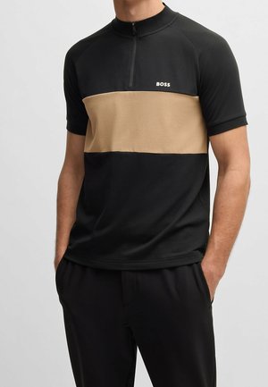 Kurzarm-Polohemd mit einem Halbreißverschluss, das einen schwarzen Oberteil und einen sandfarbenen horizontalen Streifen über der Brust zeigt. Hergestellt aus einem glatten Stoff.