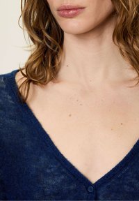 Granatowy, dziany kardigan z dekoltem w kształcie litery V. Posiada miękki, teksturowany materiał oraz jeden guzik.