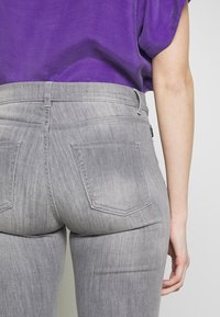 Grå denimjeans med en mjuk textur och subtila slitningar; har två bakfickor och en midjehöjd i medelhöjd.