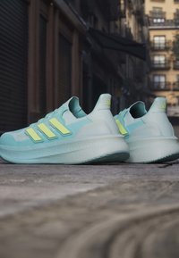 Hele sinised ja kollased Adidas jooksujalatsid, mis on paigutatud linnatänava kõnniteele, taustal on hooned.