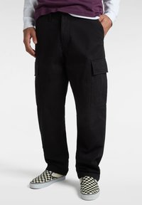 Schwarze Cargo-Hosen mit entspannter Passform, ausgestattet mit Seitentaschen, strapazierfähigem Stoff und glatter Textur. Kombiniert mit karierten Slippern.