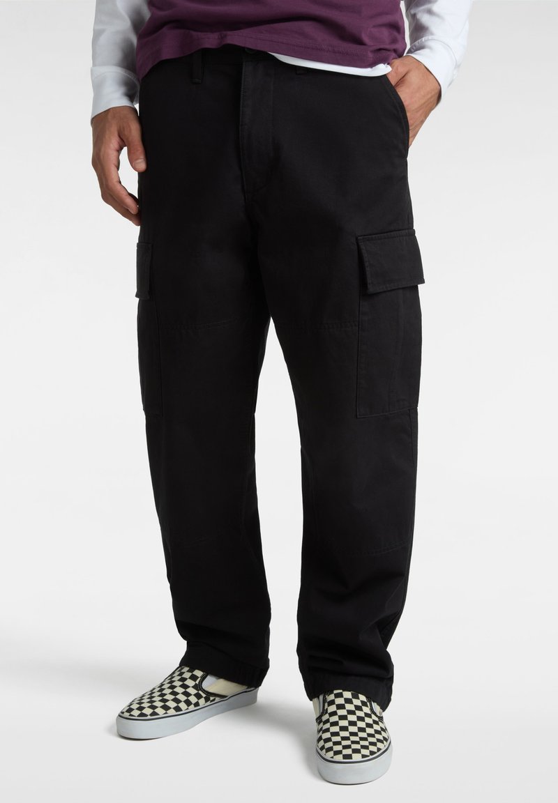 Schwarze Cargo-Hosen mit entspannter Passform, ausgestattet mit Seitentaschen, strapazierfähigem Stoff und glatter Textur. Kombiniert mit karierten Slippern.