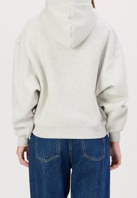 Šedá mikina s kapucí a volným střihem, vybavená klokaní kapsou a žebrovanými manžetami, doplněná tmavě modrými džíny s vysokým pasem.