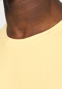 T-shirt giallo a girocollo realizzato in tessuto morbido. Presenta una texture liscia e un design semplice, privo di decorazioni.