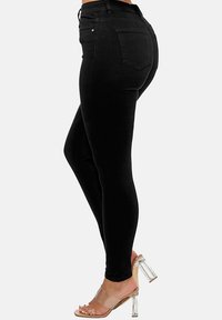 Jeans ajustados negros hechos de denim elástico, con una cintura alta, bolsillos y una textura suave. Combinados con sandalias transparentes de tacón cuadrado.