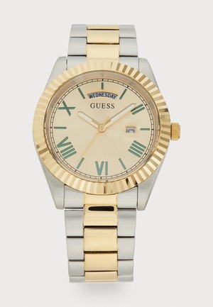 Montre en acier inoxydable doré et argenté avec un cadran rond beige, des chiffres romains verts et un affichage de la date. Possède une lunette texturée dorée et un bracelet.
