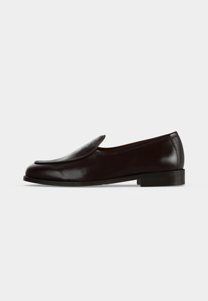 Mocassin en cuir noir sans lacets avec un talon bas et une finition lisse, vu de côté sur fond blanc.