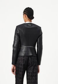 Černá kožená bunda s přiléhavým střihem, s peplum designem, viditelnými švy a stříbrným zipem na pase.