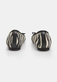 Fekete-fehér zebra mintás balettcipők lekerekített orral, puha textil felsőrésszel és fekete bőrkiegészítőkkel a saroknál és a masni részén.