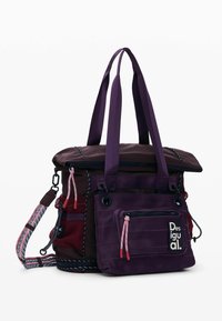 Lilla shopper-taske med flere rum, der har lynlåslukning, justerbar rem og kontrasterende strukturerede detaljer. Brandlogo synligt.