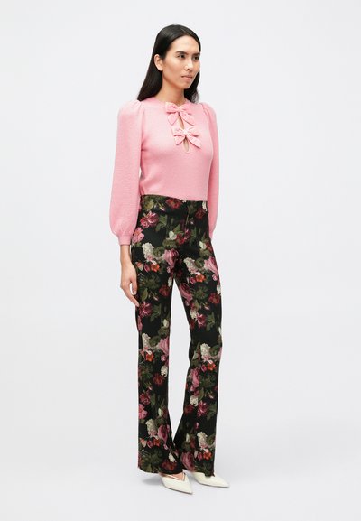 Ružový pletený sveter s nafúknutými rukávmi a mašľou na výstrihu, v kombinácii s čiernymi širokými nohavicami s kvetinovým vzorom. Béžové lodičky.