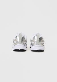 Białe buty sportowe z srebrnymi akcentami, siateczkowymi wykończeniami, wyprofilowanym piętem i czarnymi gumowymi podeszwami. Posiadają pętelkę na tyle dla łatwego zakładania.