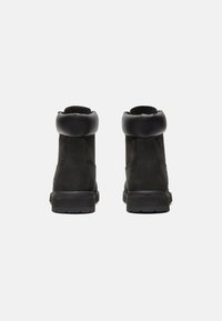 Bottines en daim noir avec un col arrondi, une tige en cuir texturé et une semelle en caoutchouc avec des motifs de grip.