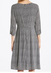 Vestido estampado en blanco y negro con mangas tres cuartos, cintura fruncida y diseño de falda acampanada, que presenta un escote redondo y cierre de botones.