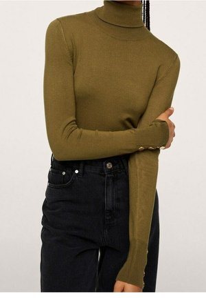 Pull à col roulé vert olive avec des manches longues, légèrement ajusté, présentant des boutons décoratifs sur les poignets, assorti à un jean noir taille haute.