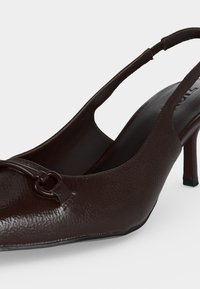 Escarpin slingback en cuir texturé marron foncé, bout pointu, petit talon kitten et boucle métallique décorative à l'avant.