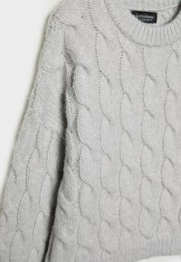 Pull en laine gris clair à torsades, manches longues et col rond côtelé, suspendu sur un fond blanc.