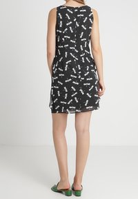 Svart ärmlös klänning med ett mönster av trollsländor i vitt, med en figursydd design och subtil textur, tillsammans med gröna slidessandaler.