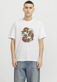 Hvid bomulds t-shirt med et centralt motiv af fire kranier omgivet af røde blomster og gule stjerner. Løs pasform og korte ærmer.