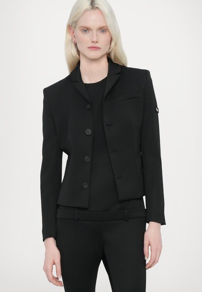Black tailored blazer with structured design, single-breasted closure, and four buttons. Features a flap pocket and slim fit silhouette.