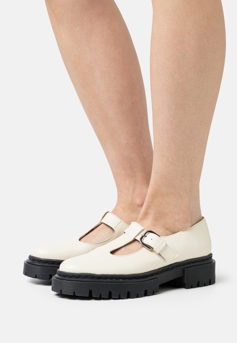 Chaussures Mary Jane blanches en cuir avec une sangle à boucle, un design découpé et des semelles en caoutchouc noir chunky, présentant des détails texturés.
