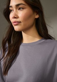 Hellpurpurfarbenes Sweatshirt mit rundem Halsausschnitt, gerippten Bündchen und weichem Material, teilweise auf der Schulter und dem Hals eines Models sichtbar.