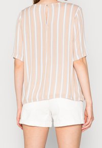 Beige randig topp med ljusblå vertikala ränder, korta ärmar, en nyckelhålsdetalj baktill och en avslappnad passform, tillsammans med vita shorts.