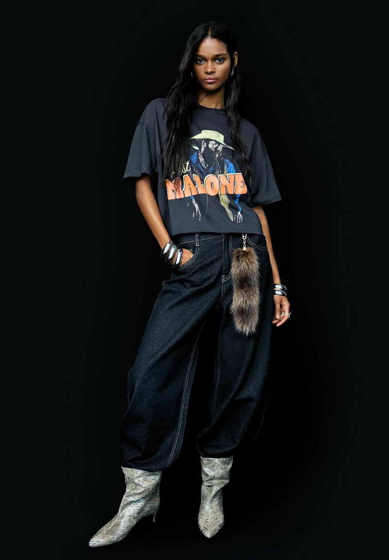 Black graphic t-shirt featuring a colorful print, paired with wide-leg dark denim jeans. Notable fur accent attached to the waistband. Silver accessories.