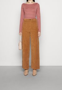 Randig långärmad topp i rosa och brunt, matchad med höga vida corduroybyxor i brunt. Beiga klackar och liten handväska.