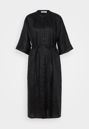 Abito nero in lino con bottoni frontali, maniche corte a kimono, una cintura in vita e una silhouette fluida. Texture liscia e design minimal.