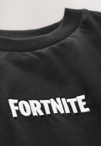 Sort sweatshirt med ribbet krave og hvidt broderet "FORTNITE"-tekst på fronten. Blødt stof med en glat tekstur.