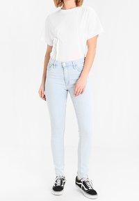 Jeans ajustados de color azul claro con una cintura alta, combinados con una camisa blanca de manga corta y zapatillas negras con suela blanca.