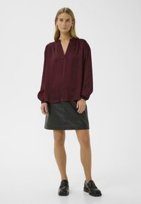 Burgundy silk blouse with a V-neck and gathered sleeves, paired with a black leather mini skirt and black loafers for a polished look.