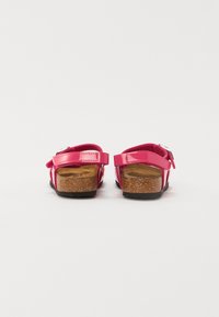 Rosa glänsande lädersandaler med korkfotbädd, justerbara remmar och en texturerad sula. Bakifrån visas spänne och remmdetaljer.