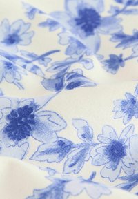 Vitt tyg med ett blått blommönster, som har intrikata blommor och blad, mjuk textur och en slät yta.