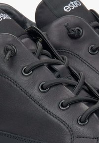 Czarne skórzane sneakersy posiadają okrągłe sznurowadła, metalowe oczka i wyściełany kołnierz. Nazwa marki jest widoczna na języku buta.