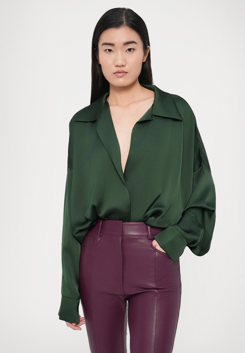 Green satin blouse with a deep v-neck and oversized sleeves, paired with high-waisted burgundy faux leather pants. Smooth texture and sleek fit.