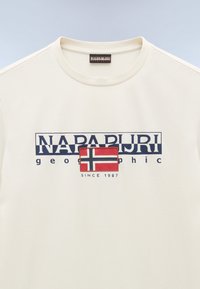 Kræmfaret bomulds T-shirt i cremefarve med et trykt logo med det norske flag, teksten "Napapijri geographic" i blåt, og "siden 1987" nedenunder.