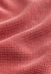 Tissu texturé en forme de gaufre, de couleur rose poudré douce. Le matériau présente un motif en grille subtil avec une apparence lisse et fluide.