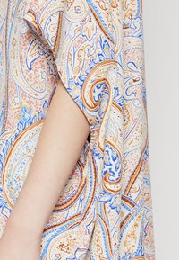 Lahki material s paisley vzorom v oranžni, modri in kremni barvi, z ohlapnim krojem in stranskim razporkom na rokavu.