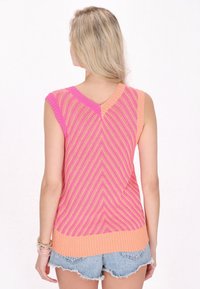 Stickad ärmlös topp med V-ringning, mönster i rosa och orange zigzag, ribbad textur och kontrasterande orange fåll.