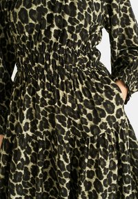 Green and black leopard print dress with an elastic waist, long puffed sleeves, and tiered skirt, featuring a textured fabric finish.