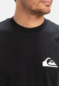 Black cotton T-shirt with a round neckline and short sleeves. Features a small white logo on the left chest area.