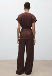 Costum compus din două piese de culoare burgundă, având un top texturat cu mâneci scurte și pantaloni cu picioare largi. Accesorizat cu un talie legată și o brățară.