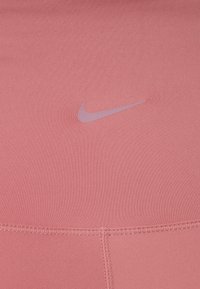 Haut de sport rose en tissu extensible, avec un logo Nike violet clair sur le devant et une texture côtelée horizontale.